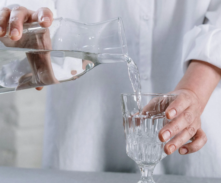 A person is pouring water into a glass on a table.